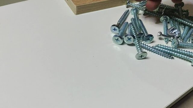 A man's hand put minifix screws from set of tepered screws on wooden table