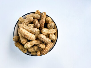 Unpeeled peanuts in a white bowl, on a white background. Unpeeled peanut isolated.