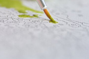 Close-up of a paintbrush adding green to a detailed paint-by-numbers canvas.