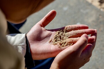 Hands Holding Sand Outdoors. Close-up image of hands carefully holding fine grains of sand under natural sunlight. 