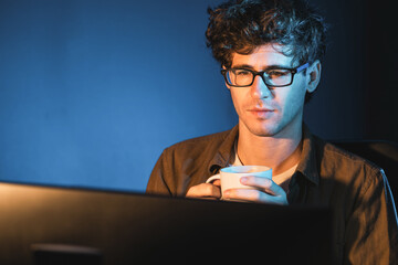 Young businessman working creative startup project job, drinking hot drink with coffee or tea while focusing on pc at neon light modern office with portrait view. Thinking marketing plan of. Gusher.