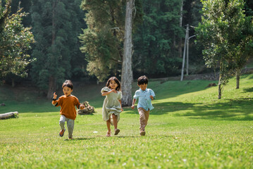 Obraz premium Three joyful children are playfully running around in a lush, green park basking in the sun