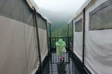 A person wearing a raincoat stands in between two glamping tents on a very misty and foggy day