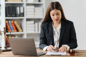 Focused Legal Professional: A young Asian female lawyer meticulously reviews documents at her desk,...