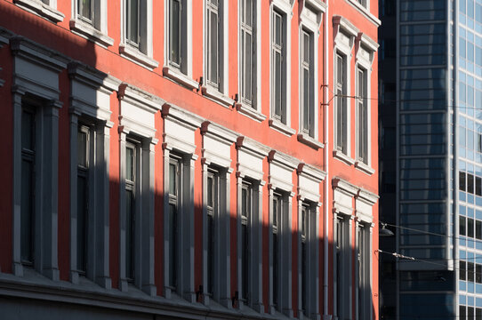 Partially shadowed pink old building  with row of tall windows next to a modern office building