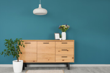 Wild flowers in vase on chest of drawers and decorative tree in room