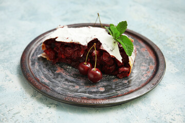 Plate with piece of tasty cherry strudel on blue grunge background, closeup