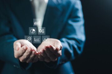 Control and business processes management concept. Businessman holding analytics icon on virtual screen for efficient operation and increased profits.