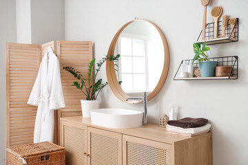 Modern sink, chest of drawers, folding screen and laundry basket in interior of bathroom