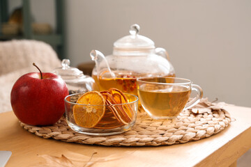Wicker mat with teapot, cup of tea, apple and dried oranges on table in room. Closeup