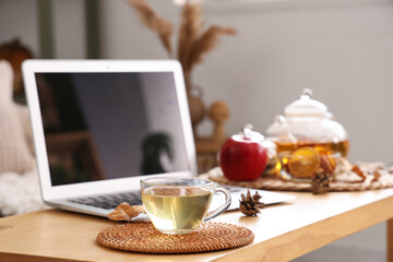 Cup of green tea near laptop on table in room. Closeup