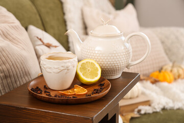 Teapot, cup of green tea, lemon and dried cloves on table in room. Closeup