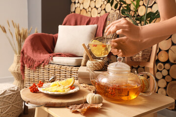 Female hands with cup of green tea near plate with lemon and rowan on table in room. Closeup