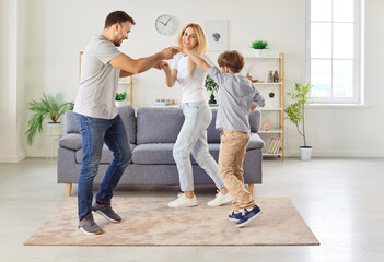 Mother, father, and little son enjoy leisure time dancing to music together at home. The happy family creates joyful memories while playing and bonding through active and fun activities.