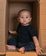 Fototapeta premium A cute baby explores a cardboard box, displaying curiosity and innocence in their actions