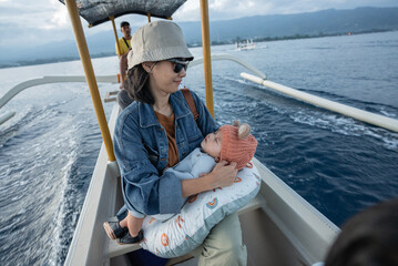 A woman is gently holding a small baby while sitting on a boat that is floating in the vast ocean under the clear blue sky