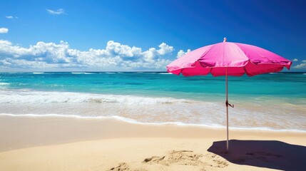 A pink parasol casting shade on a sunny beach, with the ocean waves in the background