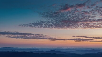 Fototapeta premium A breathtaking view of mountain ranges at sunset, with layers of blue hues and a warm orange sky. Silhouettes of mountains against a vibrant sunset sky