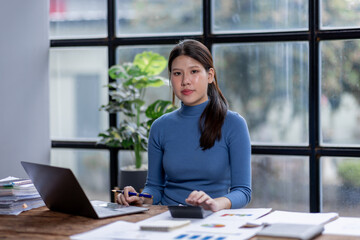 Asian Business woman using calculator and laptop for doing math finance on an office desk, tax, report, accounting, statistics, and analytical research concept
