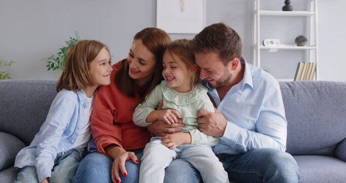 Happy family portrait, friendly loving cheerful couple of parents and cute children on cozy sofa, enjoying family leisure at home smiling, laughing together, looking at camera, positive relationship 