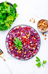 Crispy raw vegan salad with red cabbage, pomegranate, walnuts and parsley, white background, top view