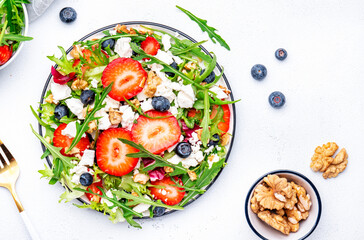 Foodie food salad with strawberry, ricotta cheese, arugula, blueberries and walnuts on white table, top view