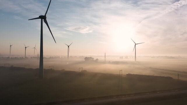 Wind turbines generating electricity in morning fog while a train passes by