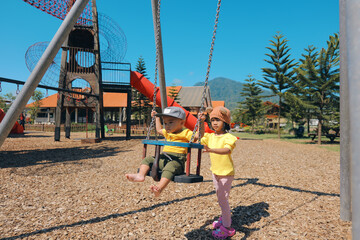On a beautiful sunny day, children are enjoying playing on swings in a colorful, lively playground