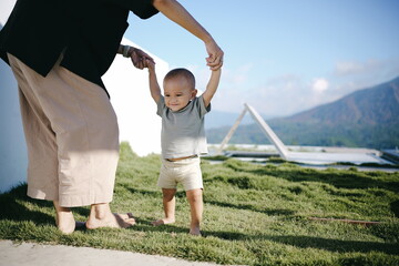 A woman is gently holding the tiny hand of a baby as they both walk together on the soft, lush...