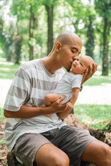 A loving father shares a tender kiss with his adorable baby in a beautiful park