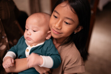 A young girl is gently and lovingly holding a small baby in her arms, showcasing a heartwarming moment of shared affection and care
