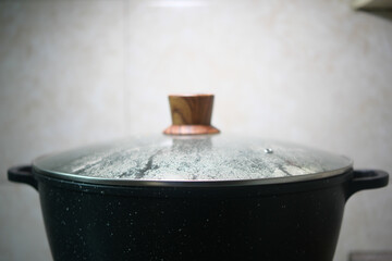 A detailed closeup image of a steaming pot that is covered with a traditional wooden lid