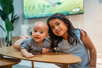 A small girl and a baby are happily seated at a table, right in front of a television, enjoying their time together in a cozy setting