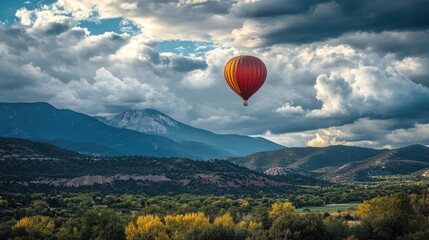 Obraz premium A single balloon rising into a cloudy sky, with a scenic mountain range in the background. No people.