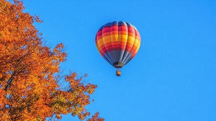 Obraz premium A solitary balloon gliding through a bright blue sky, with scenic autumn leaves below.