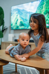 A little girl is joyfully standing next to an adorable baby who is sitting on a table, creating a delightful scene of innocence and fun