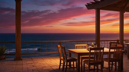 A wooden table with chairs set for dinner on a patio overlooking the ocean at sunset.