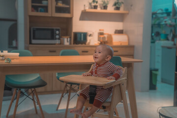 Fototapeta premium A cheerful and happy child is sitting comfortably in a high chair in a stylish kitchen design