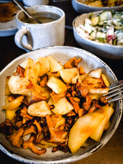 Fried potatoes with mushroom and sausage in frying pan on black stone table.