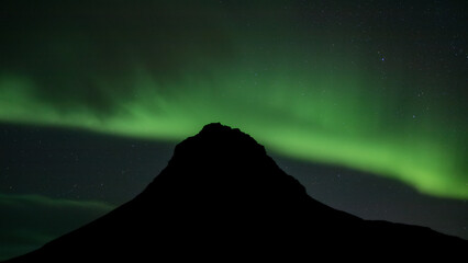 Green Northern Lights above a dark peak in Iceland