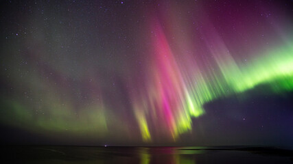 Pink and green Northern Lights / Aurora Borealis reflected in the sea