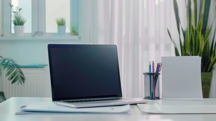 Front view laptop on white table. There is paper and a pen holder nearby. In modern office space