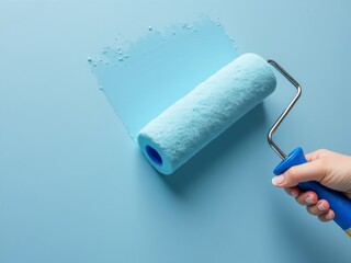 Obraz premium Hand holding a paint roller applying light blue paint on a smooth wall, representing home renovation and DIY interior decoration