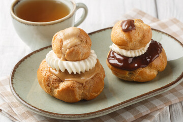 Religieuse Choux Buns filled with fluffy vanilla cream and chocolate or coffee glaze close-up in a bowl on a wooden table. Horizontal