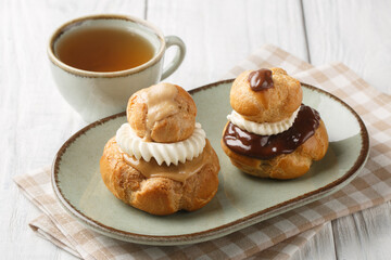 Exquisite Religieuse eclair pastry with patissiere cream with chocolate and coffee glaze close-up in a bowl on a wooden table. Horizontal