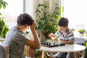 Boys brothers play chess at home at a round table on a chessboard. 