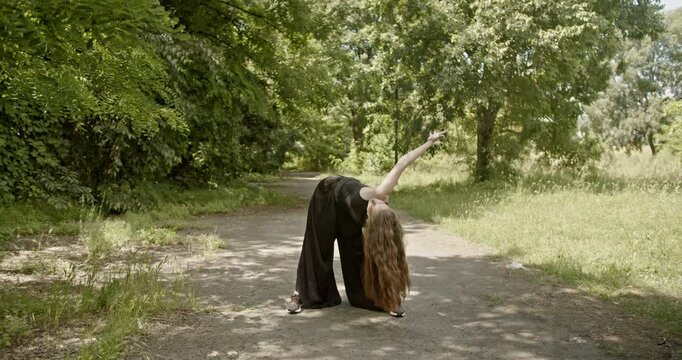 Young caucasian woman with long brown hair dances modern interpretive dance in a forest park.