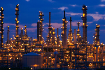 Fototapeta premium Large oil and gas refinery structures with pipelines and storage tanks, with workers in safety gear, with copy space. Industrial lighting.