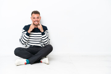 Young man sitting on the floor isolated on white background smiling with a happy and pleasant expression