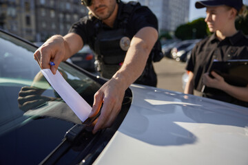Patrolman and patrolwoman putting fine for car parking in wrong place